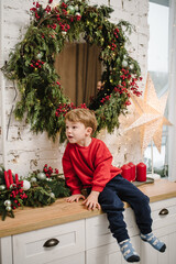 Obraz na płótnie Canvas Surprised child in red sweater sees a New Year's miracle. Serious little boy near Christmas tree at home. Merry Christmas. Сoncept of family holiday. Tree with garlands decorated interior of house.