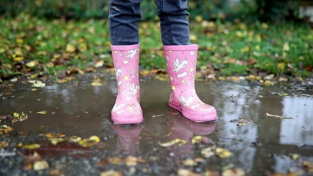 Child wearing pink rain boots with unicorns and standing in puddle on a fall day