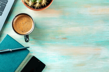 Desk, top view on a wooden blue background. Coffee, notebook, phone, plant, and laptop, overhead flat lay shot. Work layout with copy space