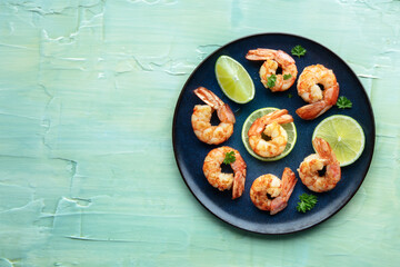 Shrimps, overhead flat lay shot on a teal blue background with copy space. Grilled shrimp with lime, spicy seafood dish