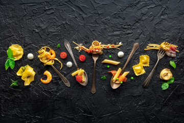 Various pasta forks. Spaghetti, fusilli, penne and other shapes of pasta, with sauce, shot from above on a dark stone table with copy space