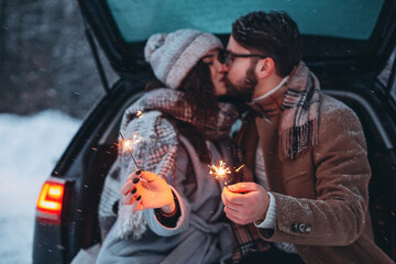Romantic couple in love celebrate together the new year with fire sparkler at the back of car. Love...
