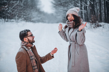 Man showing an engagement ring diamond to his amazed girlfriend in a winter park outdoor in the...