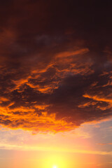 Epic dramatic red orange sunset, sunrise on storm sky with dark clouds, yellow sun and sunlight