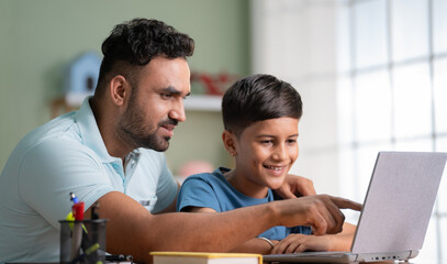 Indian father explaining or teaching from laptop to son at home - concept of family support, home education and Homework assistance