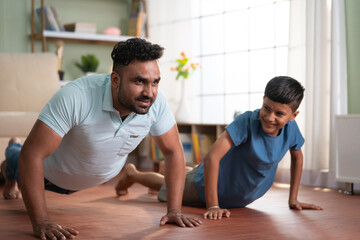 Obraz premium Joyful indian father with son doing push ups exercise at home - concept of Joyful fitness, Active lifestyle and healthy habits