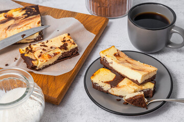 Auromatic tasty pieces of chocolate cheesecake, cup of coffee serving on the table. Glass jars of sugar, cacao powder, cutting board and cheesecake on it
