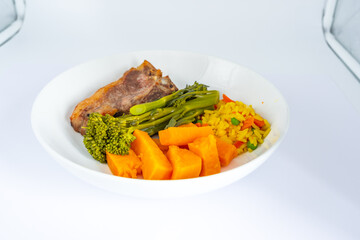 Roast lamb chop with tender stem broccoli sweet potato carrots and savoury rice served on a white plate