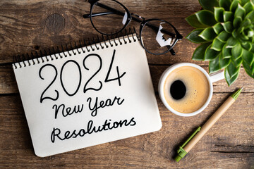 2024 New year resolutions on desk. 2024 goals list with notebook, coffee cup, plant on wooden...
