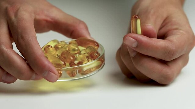 Omega 3 supplement presented on white background, hand holding capsule