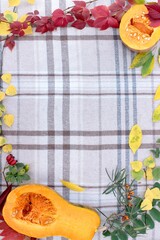 checkered beige autumn background with edible cut pumpkin and crimson yellow leaves