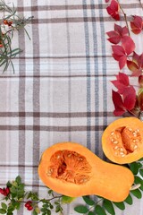 pumpkin on a cutting board, checkered beige autumn background with edible cut pumpkin and crimson yellow leaves