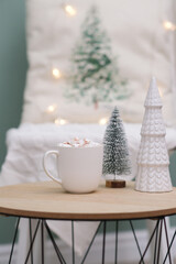 cup of cacao with marshmellows, christmas tree on coffee table on white pillow background.