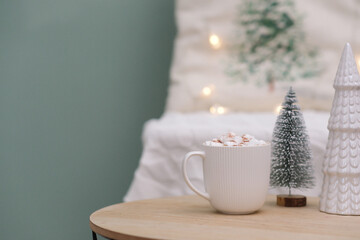 cup of cacao with marshmellows, christmas tree on coffee table on white pillow background.