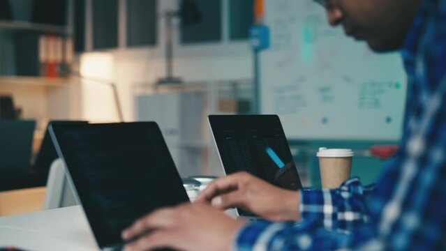 Male software engineer writing computer code on laptop in office, programming