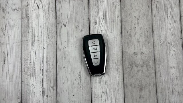 The car keys are black with metal inserts and automatic buttons placed by a white European hand on a white wood background. High quality 4k footage