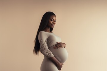 Dark-skinned pregnant woman embracing her maternity body in studio.