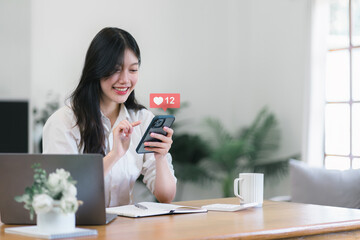Happy young Asian woman using smartphone to interact with social media icons. Social media...