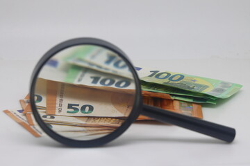 Hundred euro banknote under magnifying glass. Viewing a pile of banknotes through a magnifying glass, financial accounting and control, euro cash.