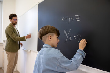 The boy answering at the maths lesson and writing on the board