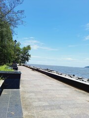 Tranquil outdoor scene with an empty sidewalk with two benches situated in front of a body of water