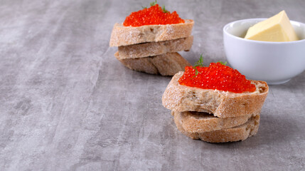 Red caviar and butter on slice of baguette on gray table. Festive appetizer. Mockup with copy space