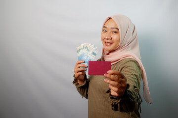 Happy beautiful Asian Muslim woman holding paper money and  showing credit card isolated on white background. ​