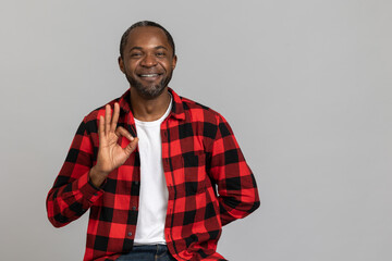 Smiling black bearded man wearing red checkered shirt showing ok sign