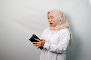 Unhappy young Asian Muslim woman wearing hijab showing empty wallet isolated on white background