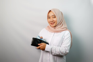 Happy Asian hijab woman excited holding money banknotes and a wallet looking at camera isolated on white background.