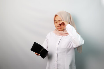 Crying young Asian Muslim woman showing empty wallet isolated on white background