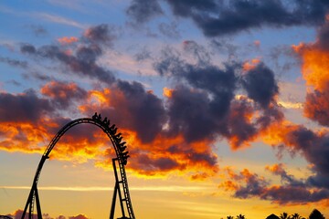 Black roller coaster is silhouetted against a vibrant orange and pink sunset sky