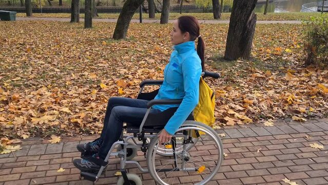 Young adult woman on wheelchair in park in autumn. Lonely disabled woman on street