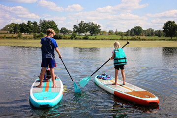 Two kids are outside on a lake on a summer day learning to stand up paddle board.