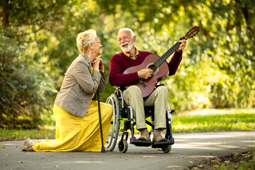 Fototapeta na wymiar Senior couple love and happiness. Elderly man in wheelchair playing guitar to his lovely wife.