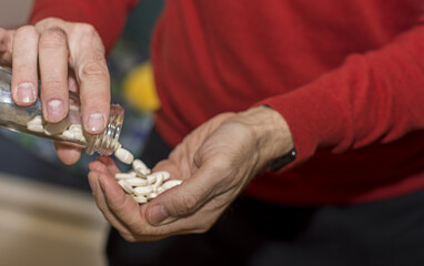 European man in red shirt pouring pills from prescription pill bottle