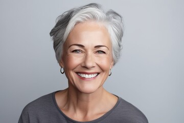 Fototapeta premium Graceful Aging: A Smiling and Happy Mature Lady Graces a Plain Grey Background, Exuding Contentment, Cheerfulness, and the Inner Peace of Retirement