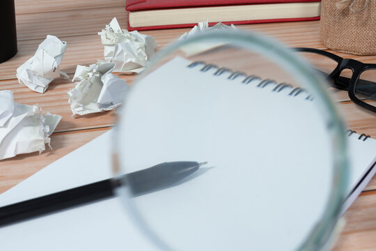 Magnifying glass on notepad and trash paper background on office desk.