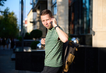 Young sporty man in a striped T-shirt walking on the street with a smartphone in hand and a trendy...