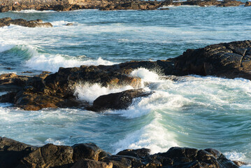 Sea waves lapping gently on the dark rocks of the beach.