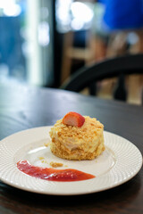 Napoleon cake, made with layers of puff with whipped cream and crumbs with Strawberry on top and sauce served on plate