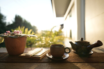 Earthenware tea cup and tea pot with brown plant pot and notebooks