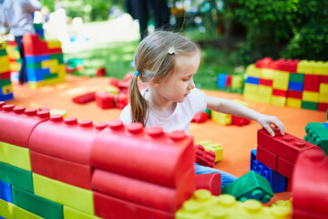 Fototapeta na wymiar Adorable preschooler girl playing with large colorful plastic construction blocks outdoors, in kindergarten or preschool