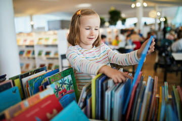 Five year old girl selecting a book in municipal library - Powered by Adobe