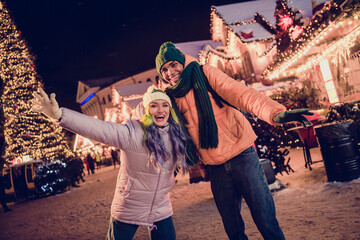 Photo of cheerful impressed african guy lady dressed coats rising arms enjoying x-mas shopping together outdoors urban fair park