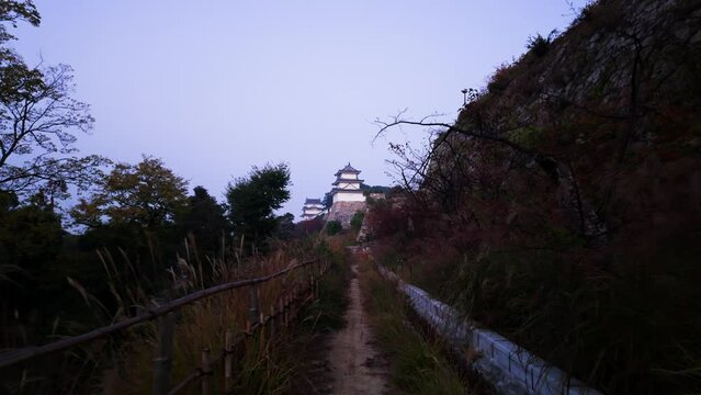 Walking dirt path in tall grass to Akashi Castle at dawn in autumn 