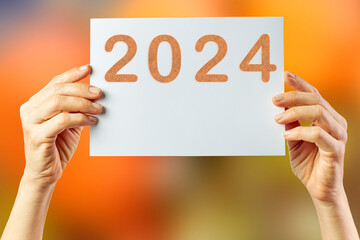 2024, Woman holding cardboard with number 2024 on orange background. Happy New Year