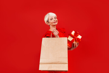 Photo of a woman with a gift box and a shopping bag against a red background, for a birthday or New Year celebration.