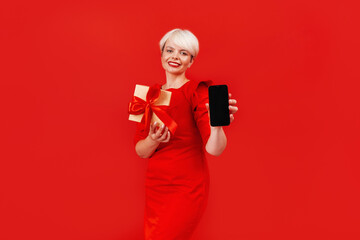 A photo of a woman wearing a red dress, holding a smartphone and a gift box for online shopping.