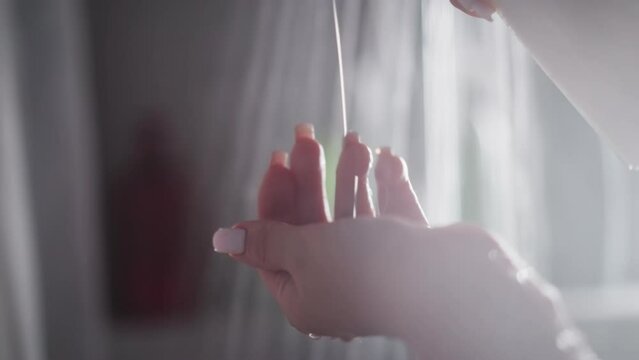 Woman flows soap on hand in shower and rubs in hand. Woman dispenses soap onto hand proceeding to rub in hands. Water cascades around woman in shower